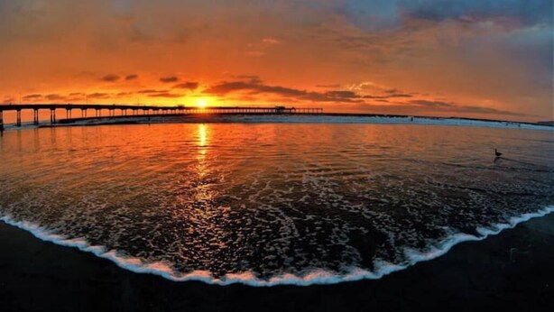 A sunset over a calm sea with a pier extending into the water.