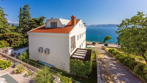 A white building with a red roof, a small balcony, and a view of the sea.