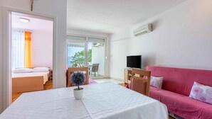 A room with a bed, a pink sofa, a TV, and a table with a plant.
