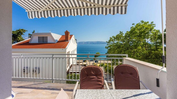 A balcony with a table and chairs, overlooking a body of water and a distant coastline.