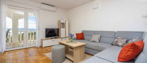 A modern living room with a grey sofa, a wooden coffee table, a TV, and a sliding glass door leading to a balcony.