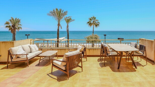 Una terraza con mobiliario exterior, vistas al mar y palmeras.
