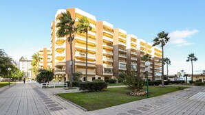 Un hotel de varios pisos con balcones, palmeras y un paseo pavimentado.