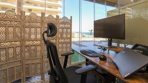 Un espacio de oficina moderno con un escritorio, una silla, una computadora y un gran ventanal con vista a la playa.