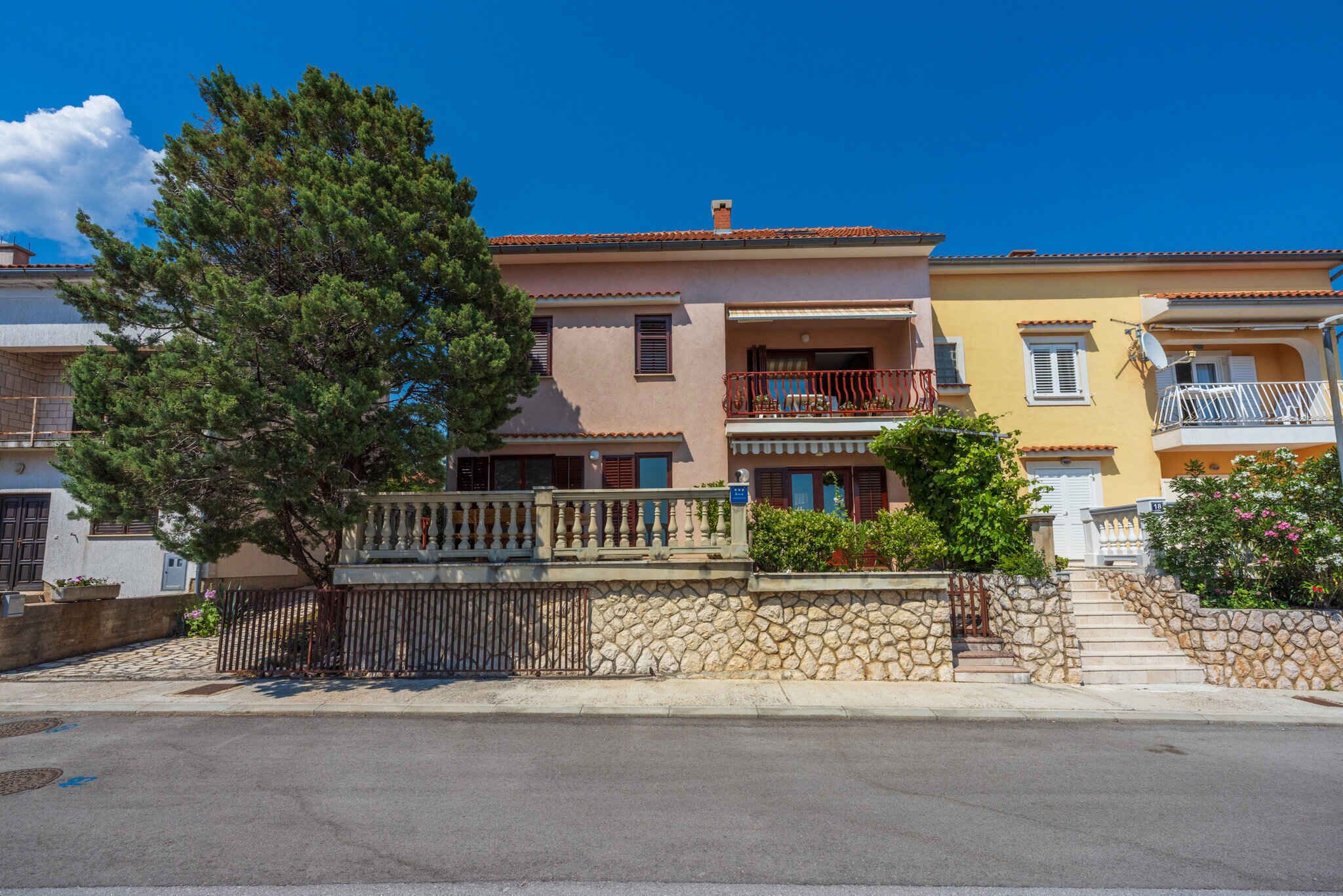 A row of Mediterranean-style buildings with stone walls, balconies, and a clear blue sky.
