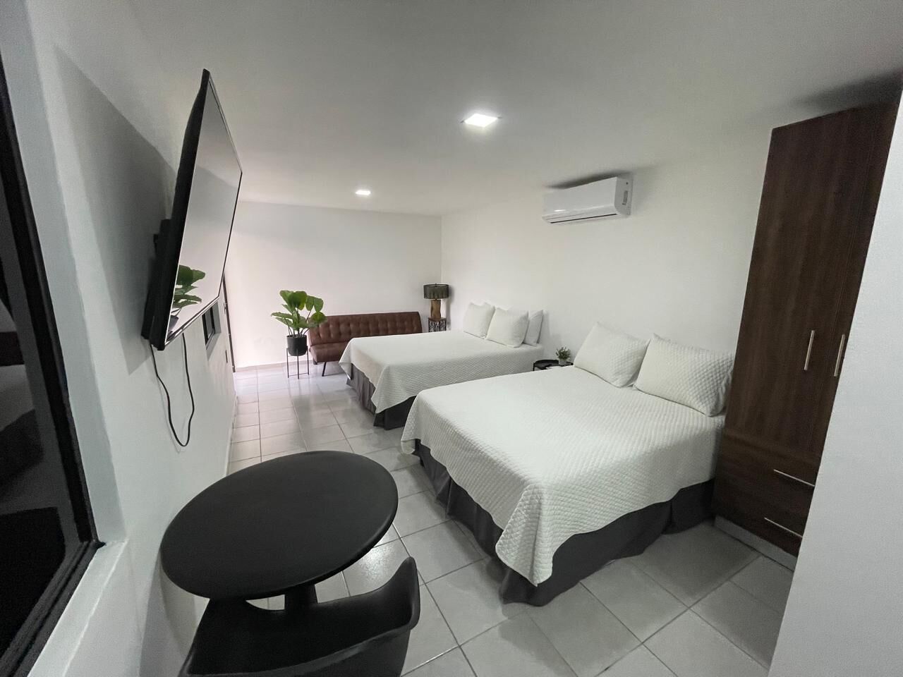 A hotel room with two beds, a TV mounted on the wall, a small table, and a wardrobe.
