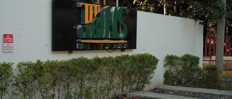 A sign with the text "THE GRINS" on a white wall, surrounded by greenery and a red sign prohibiting dumping.