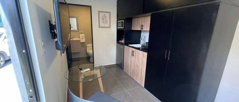A compact kitchen with a glass table, black cabinets, and a microwave.
