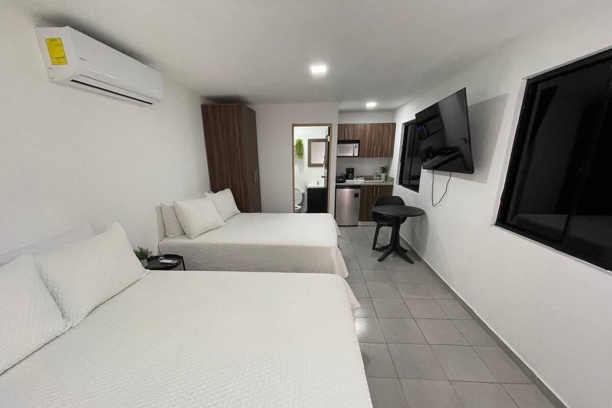 Une chambre d’hôtel avec deux lits, une télévision, un petit coin cuisine et une salle de bain visible à travers une porte ouverte.