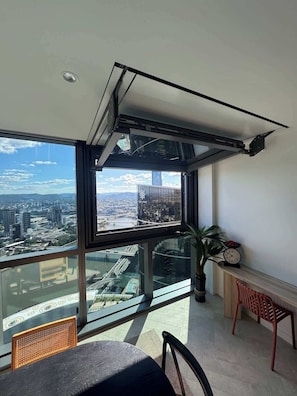 A high-rise room with a large window offering a city view, a ceiling fan, and a small table with a chair. - Dreamy Queens Wharf luxury pad w car park (Brisbane City)