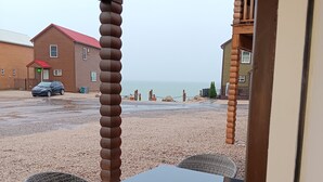 Un espace extérieur abrité avec une table et des chaises, un sol en gravier et une vue sur la mer et les bâtiments en arrière-plan.