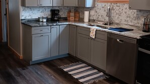 Une cuisine avec des meubles de couleur grise, un plafond en bois, une fenêtre et un tapis à rayures.
