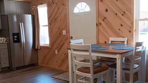 Une cuisine équipée d’un réfrigérateur, d’une table à manger avec des chaises, d’un mur en bois et d’une porte avec une fenêtre.