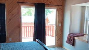 Une chambre avec un lit, une fenêtre donnant sur une terrasse en bois et une porte menant à l’extérieur.