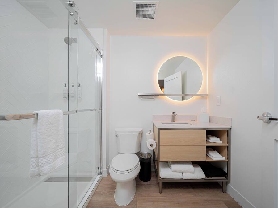 Ein modernes Badezimmer mit Duschabtrennung aus Glas, Toilette, Waschbecken mit Spiegel und Ablageflächen.
