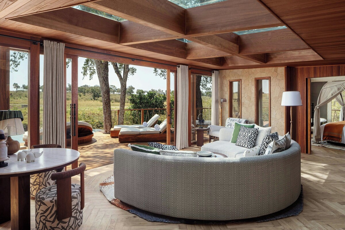 A spacious outdoor living area with a round seating area, a dining table, and a view of the surrounding landscape.