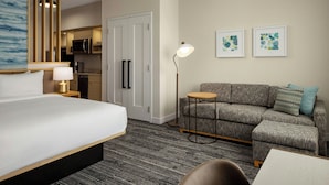 Habitación de hotel con cama, sofá, mesita, lámpara, microondas y refrigerador.