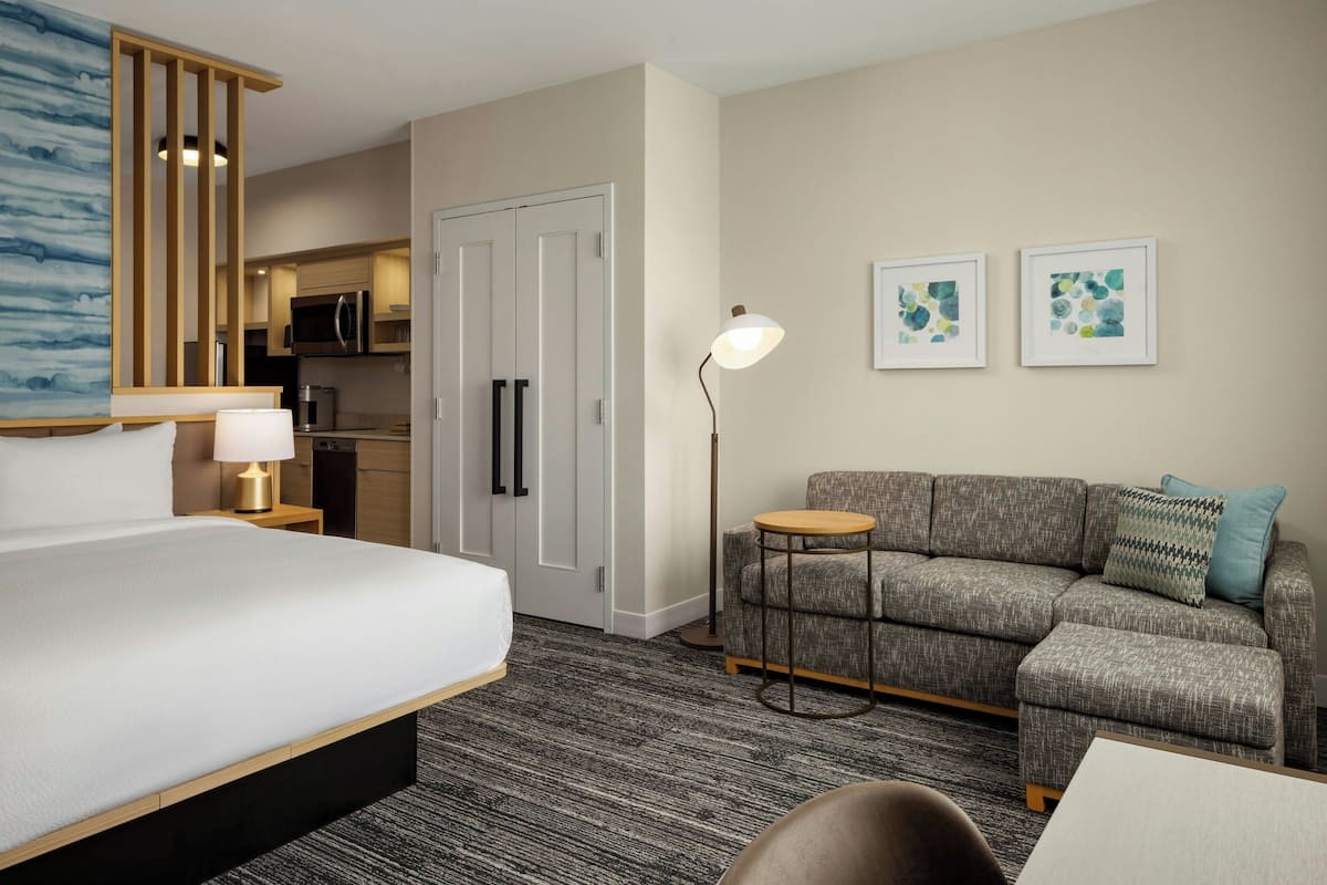 Habitación de hotel con cama, sofá, mesita, lámpara, microondas y refrigerador.