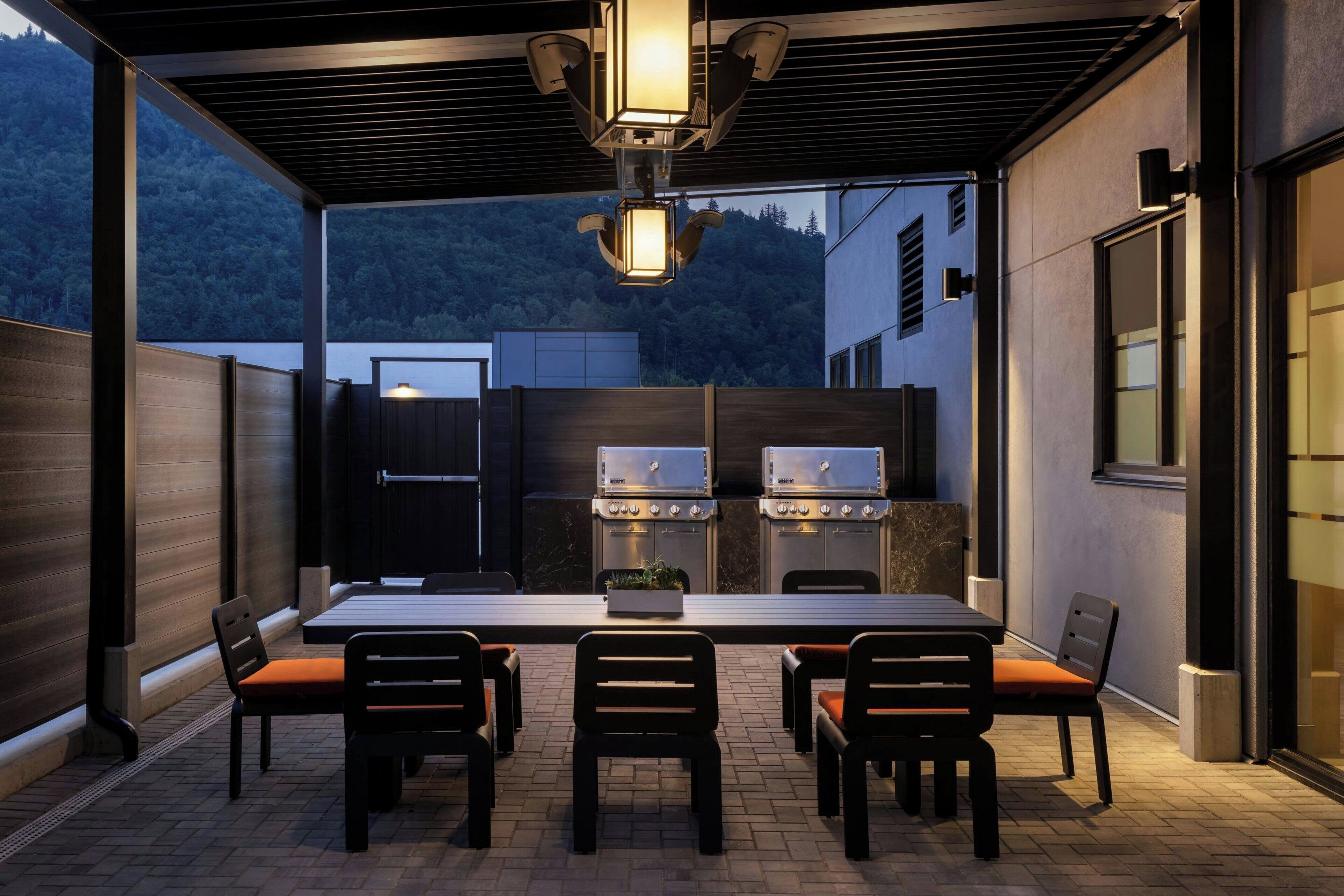 Une terrasse extérieure avec une table et des chaises, un barbecue et une vue sur une colline boisée.