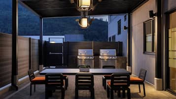 Une terrasse extérieure avec une table et des chaises, un barbecue et une vue sur une colline boisée.