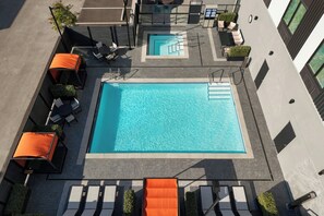 Vue aérienne d’une piscine sur le toit, avec des chaises longues et un petit escalier menant à une terrasse supérieure.