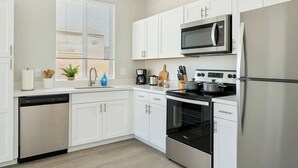 Una cocina moderna con armarios blancos, un refrigerador de acero inoxidable, un microondas, una estufa y un horno.