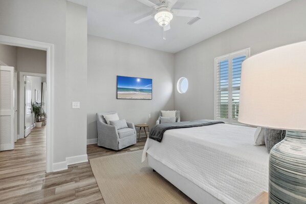 A bedroom with a bed, a chair, a small table, a painting, and a ceiling fan. - The Blue Dolphin Hideaway | Private Pool, Boat Tie-Up, Fire Pit | My Beach Getaways (Pensacola Beach)