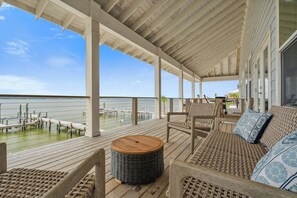 A covered outdoor deck with wicker furniture and a view of the water. - The Blue Dolphin Hideaway | Private Pool, Boat Tie-Up, Fire Pit | My Beach Getaways (Pensacola Beach)