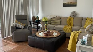 Una sala de estar con sofá, sillón, reposapiés y una mesa con objetos decorativos.