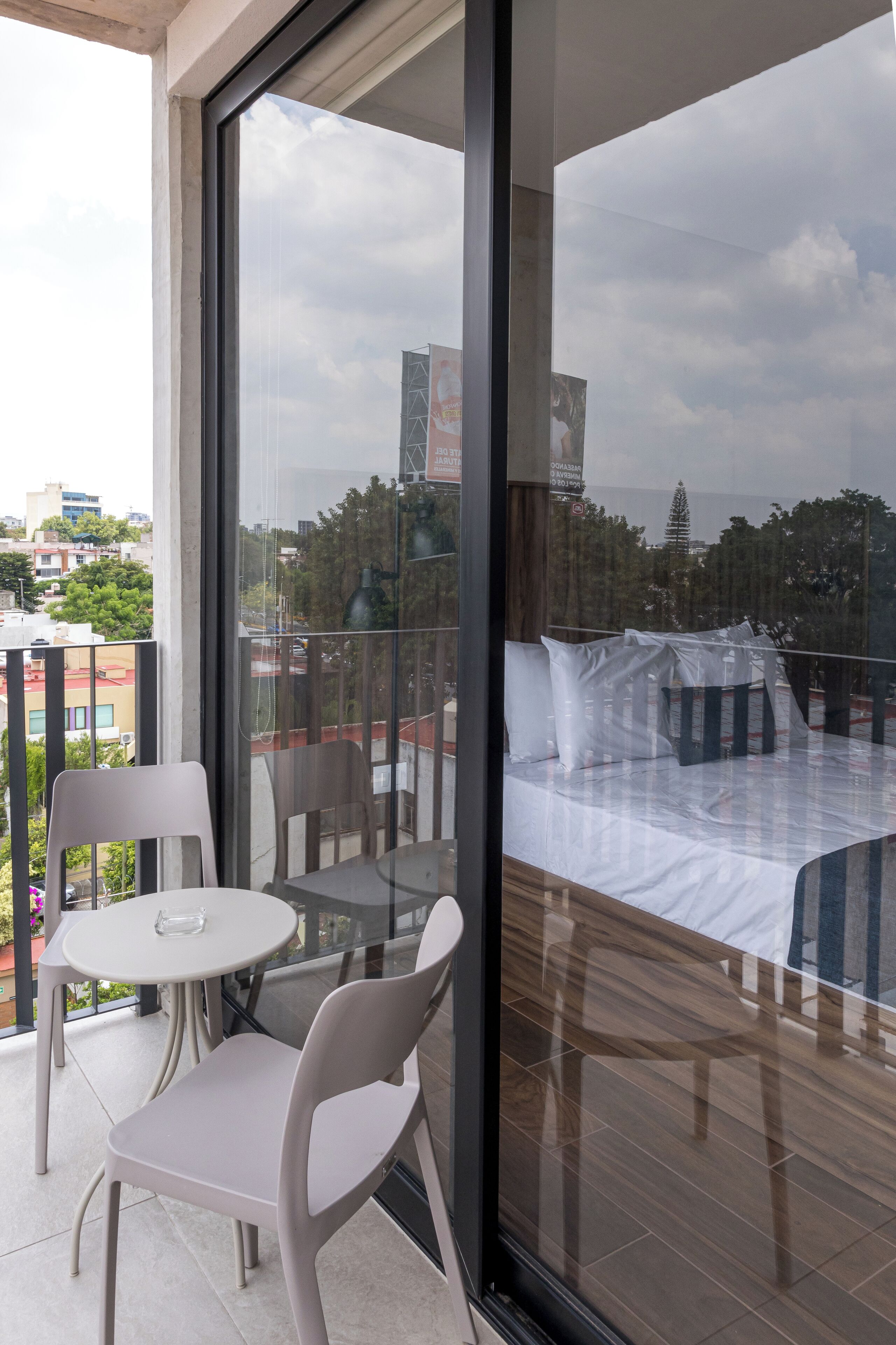 A balcony with a glass door, a bed with pillows, a small table, and two chairs.