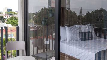 A balcony with a glass door, a bed with pillows, a small table, and two chairs.