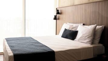 A neatly made bed with a dark throw, white pillows, and a wooden headboard in a room with large windows.