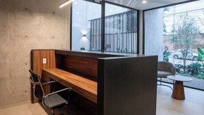 A modern office space with a wooden desk, a black office chair, and a round wooden table. - Lapso at Asís (Guadalajara)
