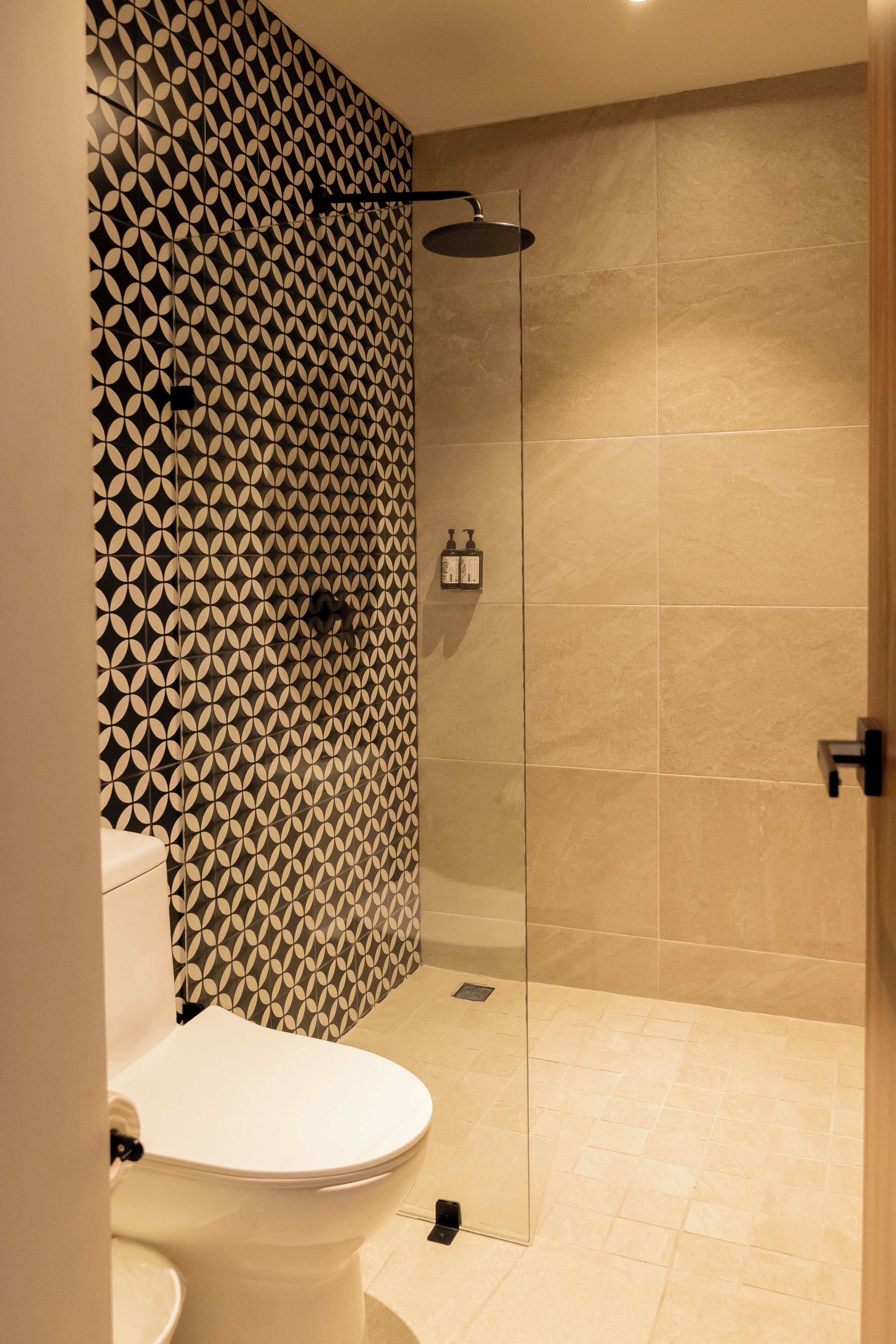 A bathroom with a toilet, a shower with a glass door, and patterned walls.