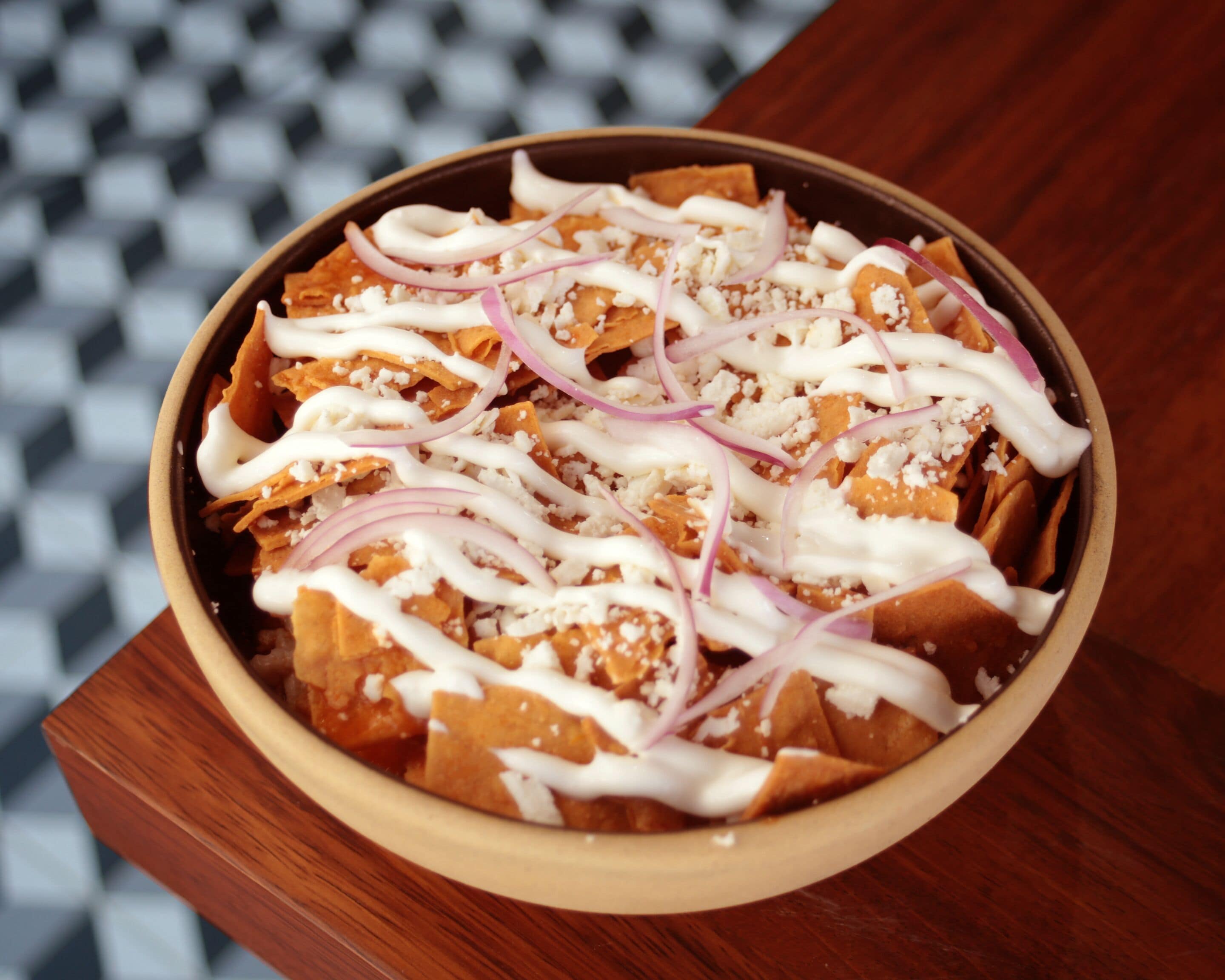 A bowl of nachos topped with cheese, sour cream, and red onions.