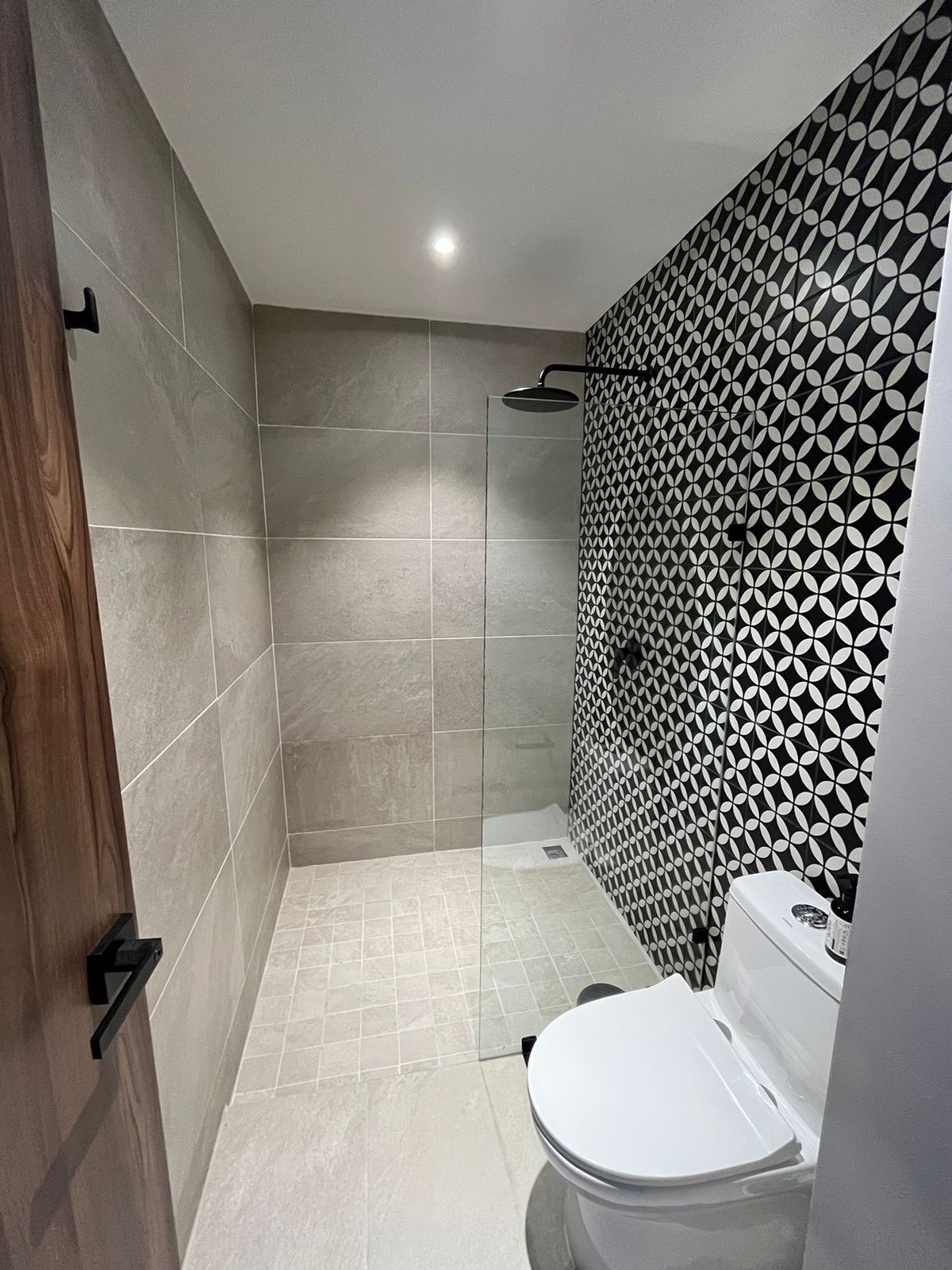 A modern bathroom with a shower, toilet, and patterned wall.
