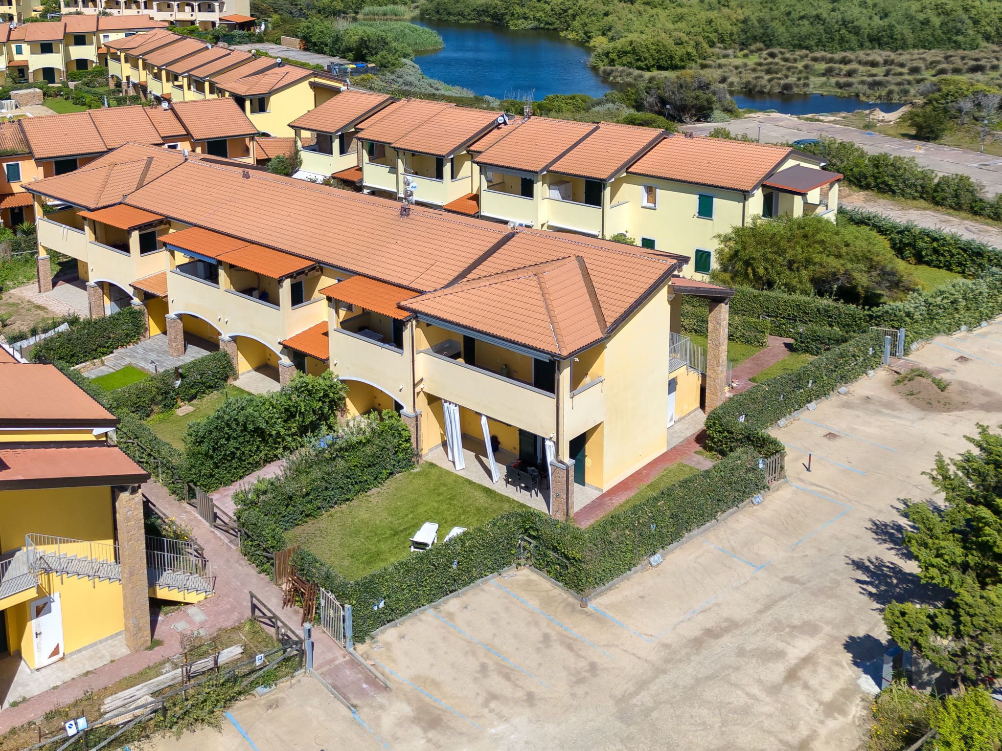 A residential building with multiple balconies, a parking area, and a body of water in the background.
