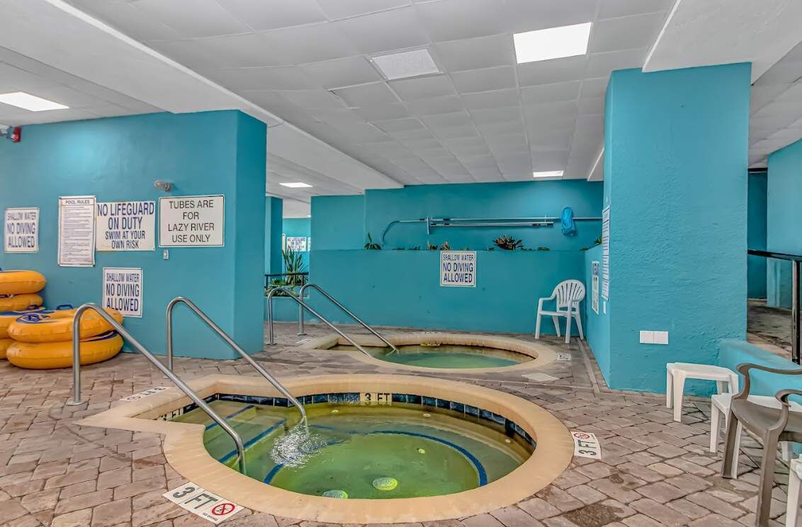 An indoor pool area with two pools, safety signs, and lounge chairs.