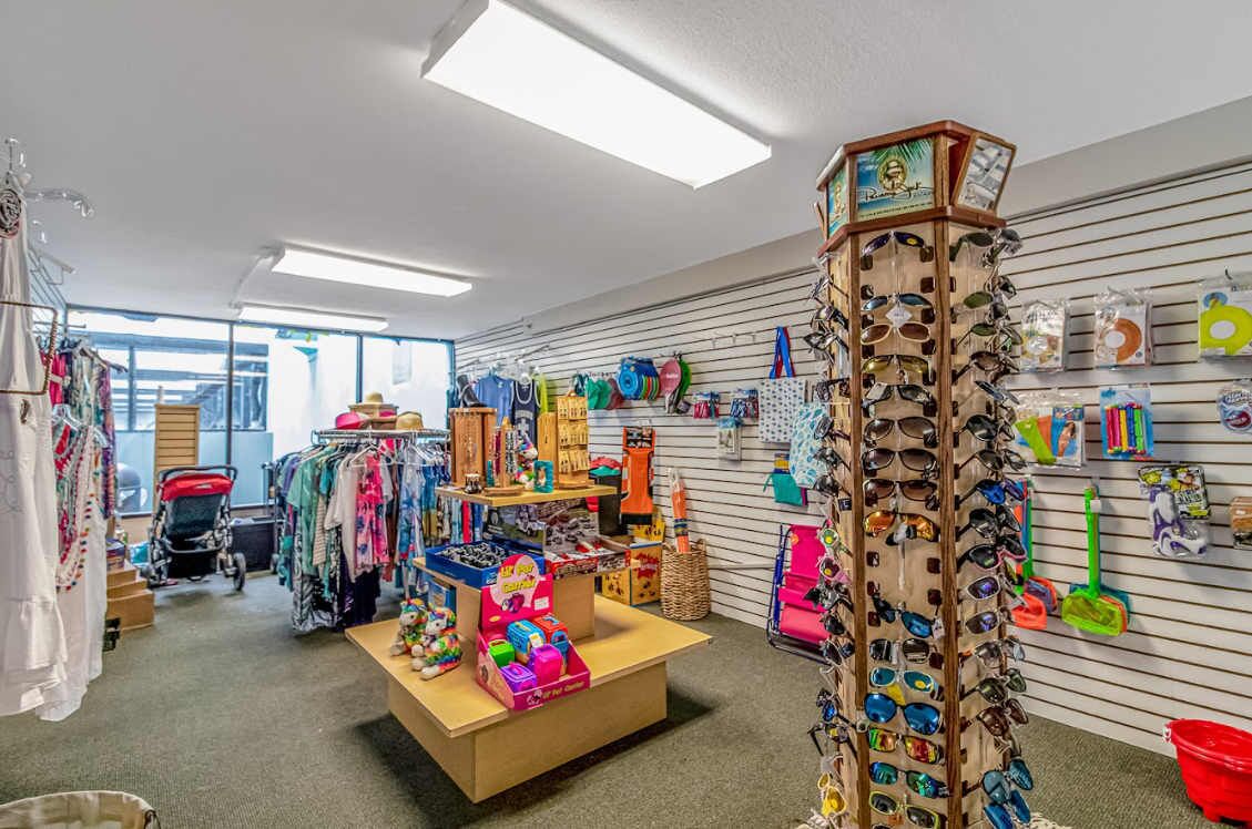 Un magasin de détail où l’on trouve des étagères remplies de lunettes de soleil, des jouets pour enfants et des présentoirs à vêtements.