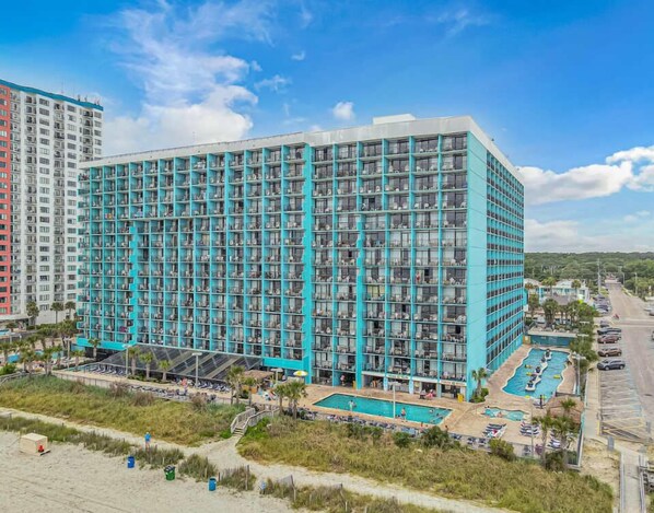 A modern hotel with a large pool area, multiple balconies, and a beachside location.