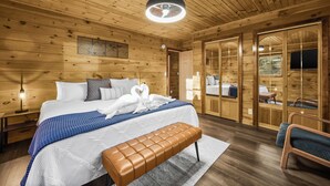 A wooden cabin bedroom with a large bed, a bench, a ceiling fan, and a sliding door leading to a bathroom. - 5BR, Heated Pool/Spa + Mtn View, Games, Karaoke, Firepit, 15 Min to PF (Sevierville)