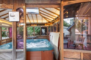 A hot tub in a wooden structure with a glass ceiling, surrounded by wooden walls and furniture.