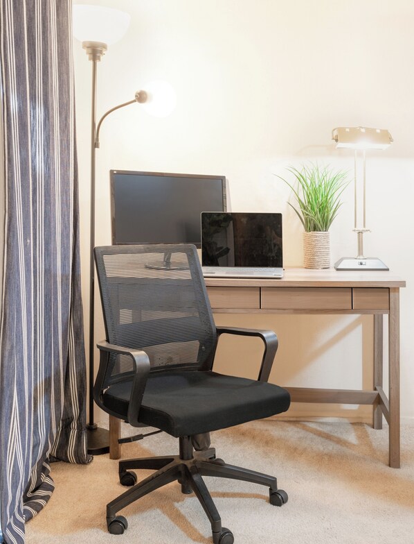 Un fauteuil de bureau moderne, un bureau avec un ordinateur portable, une lampe sur pied et une plante en pot.