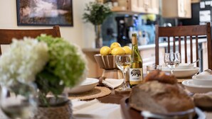 A dining table with a bottle of wine, glasses, lemons, and a bowl of fruit.