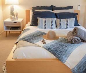 Un lit bien fait, avec une couverture à rayures, une serviette enroulée et un chapeau de paille posé sur le lit.