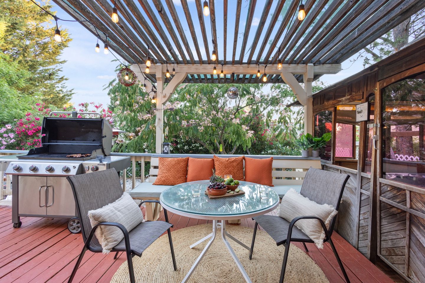 Un patio al aire libre con una parrilla, zona de estar y una pérgola con luces colgantes.