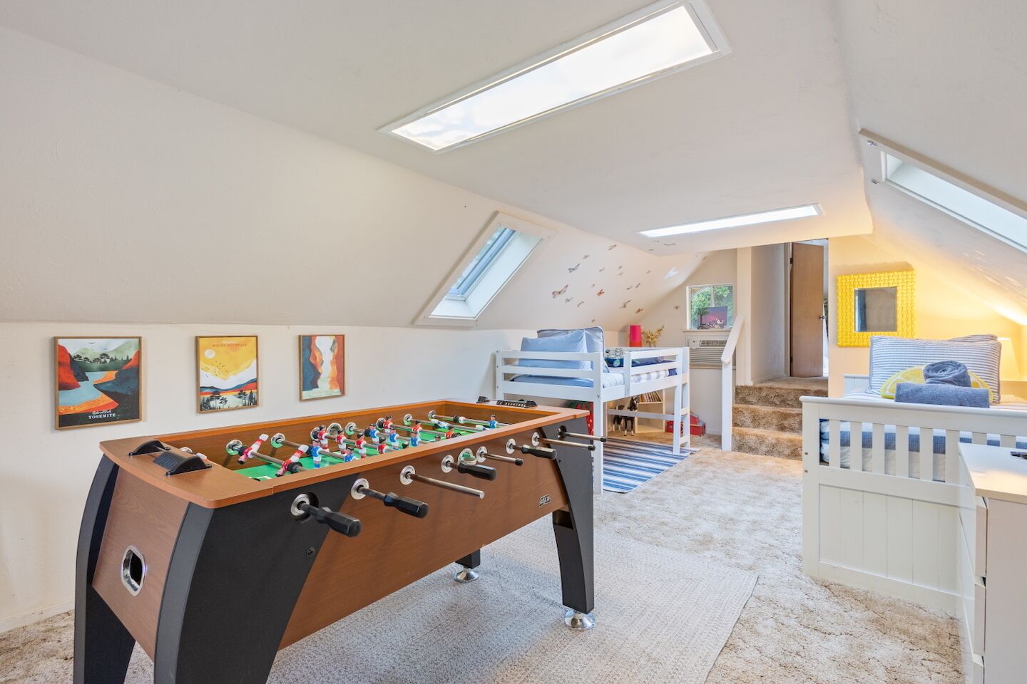 Ein Zimmer mit Tischfußball, Etagenbetten, Bildern an den Wänden und Dachfenstern.