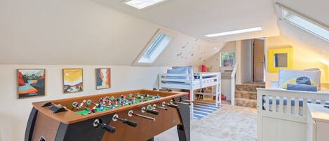 Ein Zimmer mit Tischfußball, Etagenbetten, Bildern an den Wänden und Dachfenstern.
