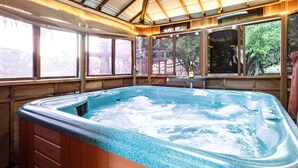 A hot tub with a wooden exterior and a view of the outdoors through large windows.