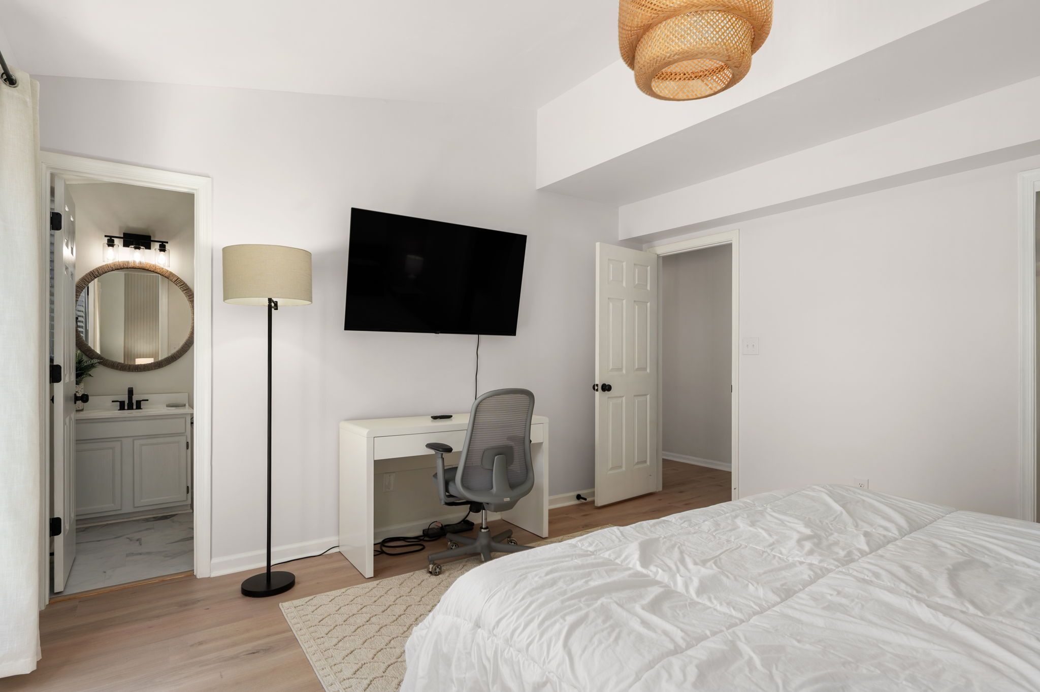 A bedroom with a bed, a desk with a chair, a TV, a lamp, and a mirror.